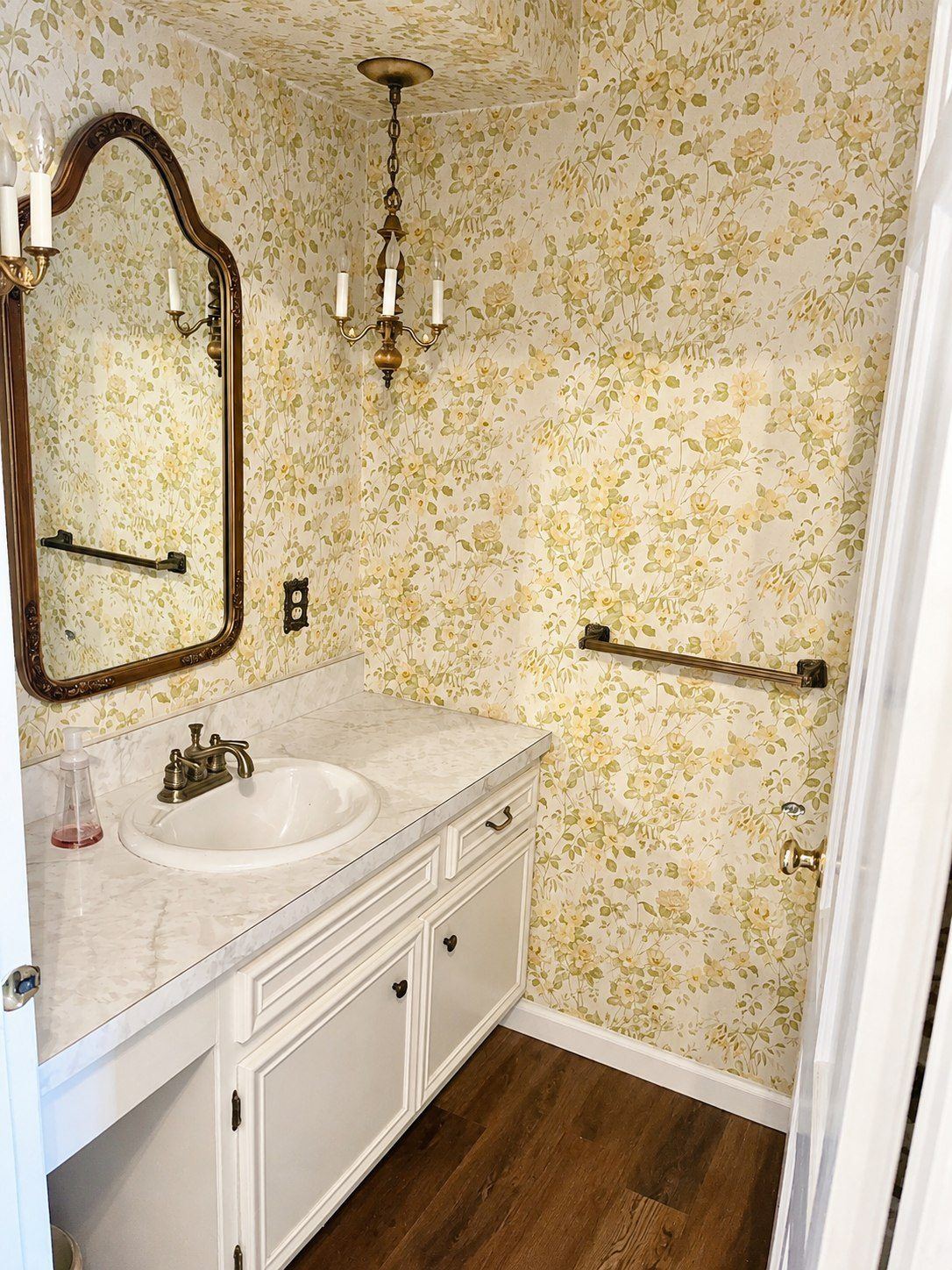 Powder room before remodel — dated floral wallpaper, brass fixtures